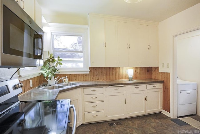 kitchen with stainless steel appliances, a sink, washer / clothes dryer, a wainscoted wall, and wood walls