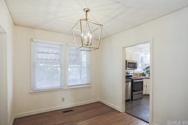 unfurnished dining area with a chandelier, dark wood-type flooring, baseboards, and ornamental molding