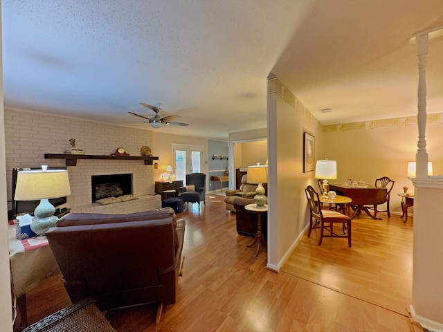 living area featuring ceiling fan, light wood finished floors, a brick fireplace, baseboards, and a textured ceiling