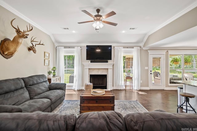 living room featuring dark wood-type flooring, a ceiling fan, a fireplace, crown molding, and baseboards