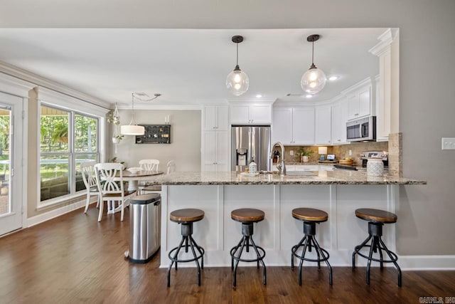 kitchen featuring appliances with stainless steel finishes, white cabinetry, light stone counters, a peninsula, and crown molding