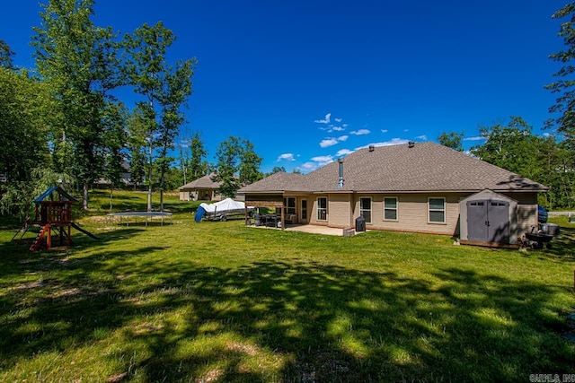 rear view of property with a trampoline, a patio, a storage unit, a lawn, and an outbuilding