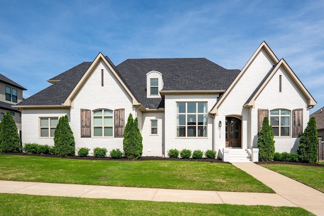 french provincial home with brick siding, a front yard, and roof with shingles