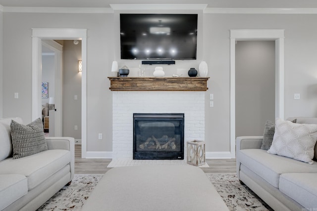 living room featuring wood finished floors, baseboards, a brick fireplace, and crown molding