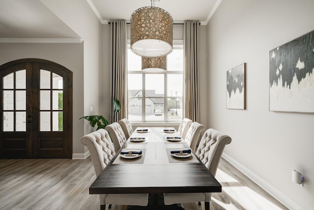 dining space featuring baseboards, light wood finished floors, crown molding, french doors, and arched walkways
