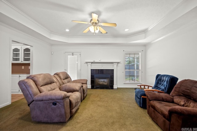 carpeted living area featuring a tray ceiling, ornamental molding, a tile fireplace, a ceiling fan, and recessed lighting