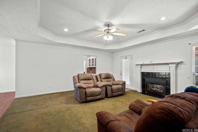 carpeted living room with a raised ceiling, crown molding, a ceiling fan, a tile fireplace, and baseboards