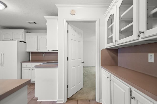 kitchen featuring white cabinets, freestanding refrigerator, glass insert cabinets, light tile patterned floors, and a textured ceiling
