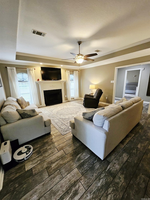 living room featuring dark wood finished floors, crown molding, a tray ceiling, a fireplace, and plenty of natural light