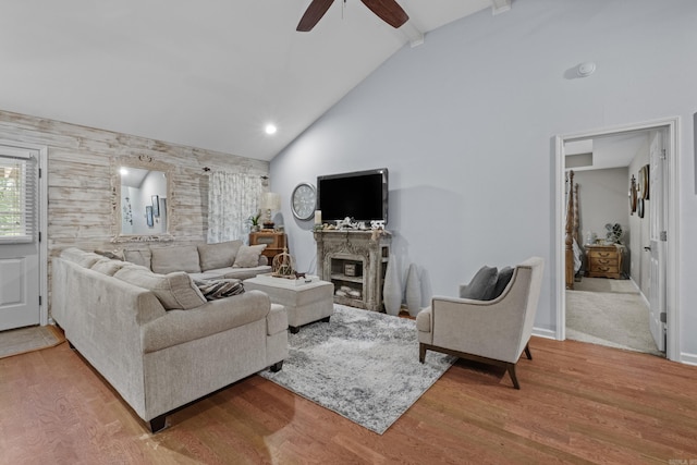 living area with a ceiling fan, wood finished floors, a fireplace, high vaulted ceiling, and an accent wall