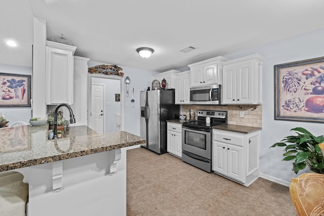 kitchen featuring appliances with stainless steel finishes, a breakfast bar, white cabinetry, tasteful backsplash, and dark stone counters