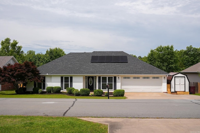 view of front facade with a shed, solar panels, a garage, driveway, and roof with shingles