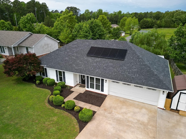 view of front of house featuring roof with shingles, roof mounted solar panels, driveway, and a front lawn