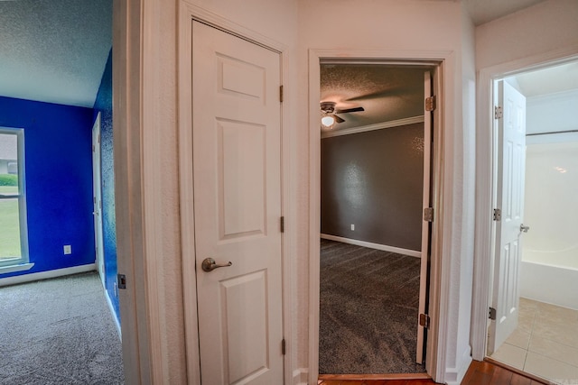 corridor featuring carpet floors, a textured ceiling, baseboards, and crown molding