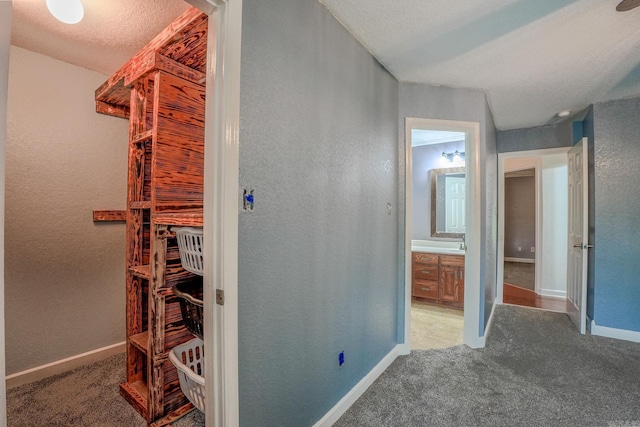 corridor with light colored carpet, baseboards, and a textured wall
