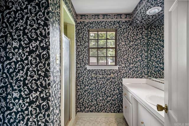 bathroom featuring wallpapered walls, baseboards, vanity, and a shower with door