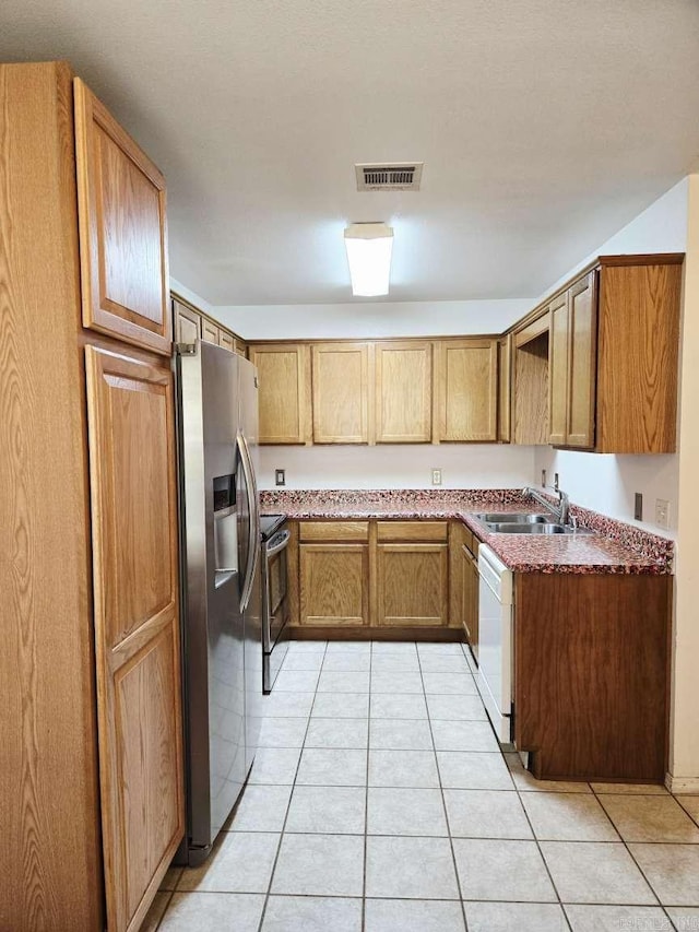 kitchen with a sink, appliances with stainless steel finishes, light tile patterned floors, and brown cabinets