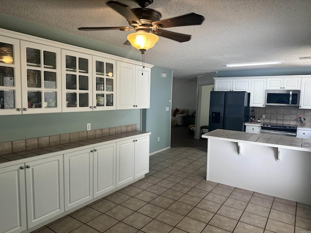kitchen featuring tile countertops, stainless steel appliances, glass insert cabinets, a textured ceiling, and tasteful backsplash