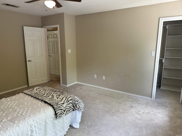 carpeted bedroom featuring a spacious closet, a closet, ceiling fan, baseboards, and a textured ceiling