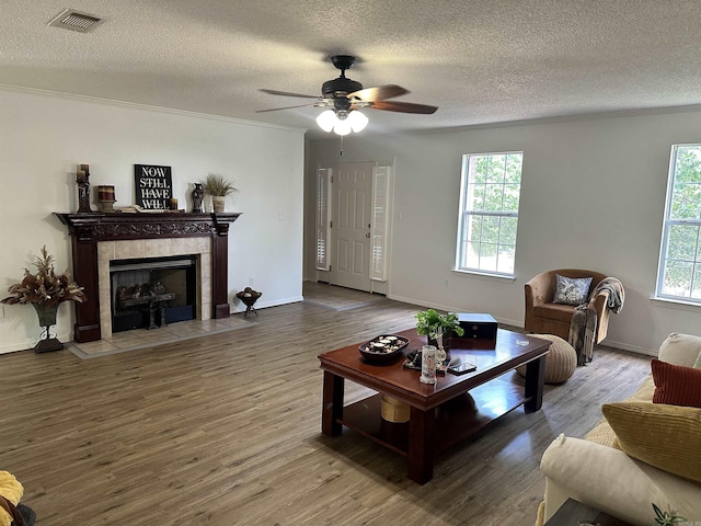 living area with a textured ceiling, wood finished floors, a tile fireplace, ceiling fan, and baseboards