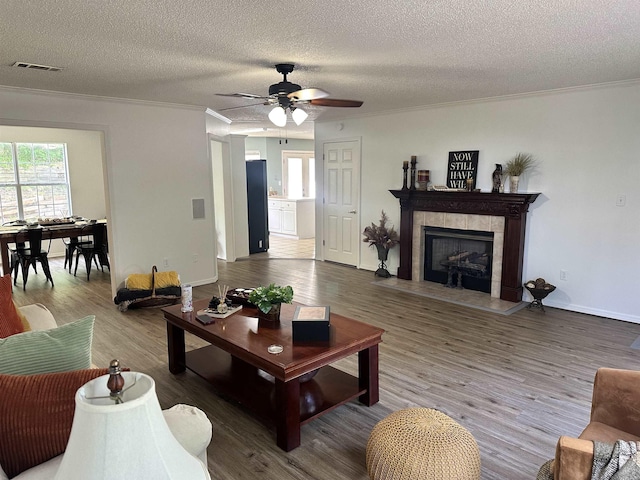 living room with crown molding, ceiling fan, a fireplace, a textured ceiling, and wood finished floors
