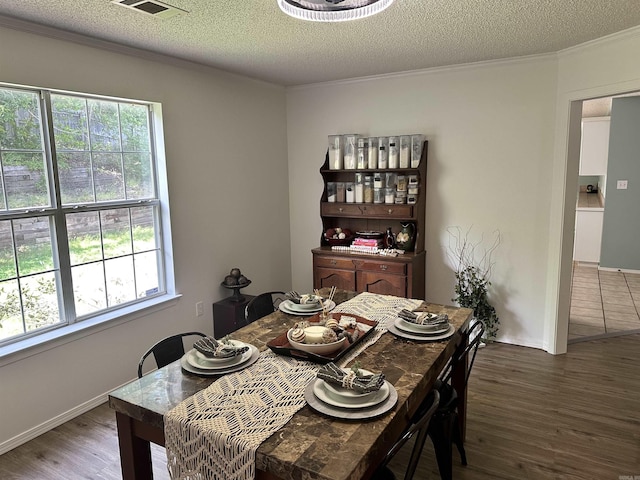 dining space featuring wood finished floors, ornamental molding, a textured ceiling, and baseboards