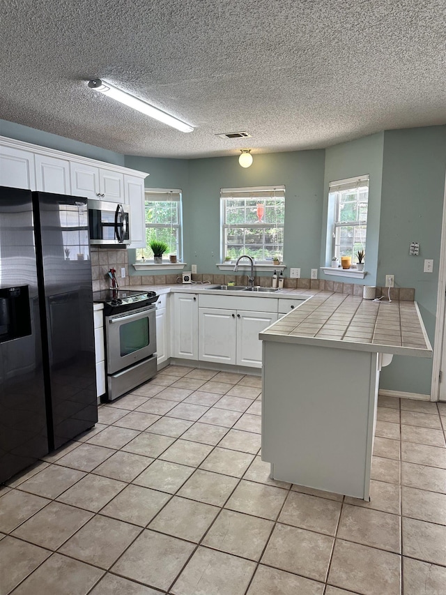 kitchen featuring stainless steel appliances, a sink, tile counters, a peninsula, and light tile patterned floors