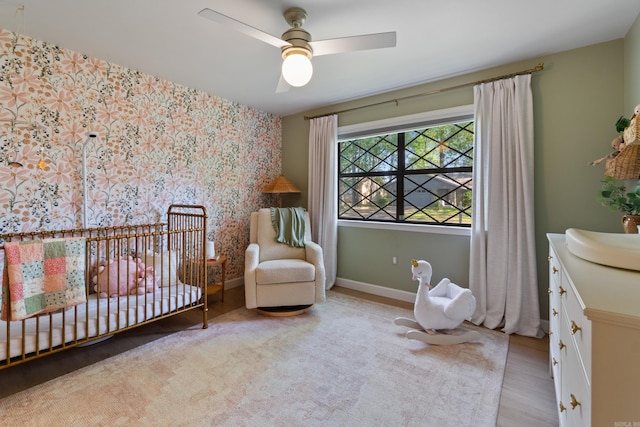 bedroom with wood finished floors, a nursery area, baseboards, and ceiling fan
