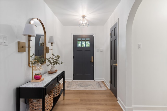 foyer entrance with light wood-style floors, arched walkways, and baseboards