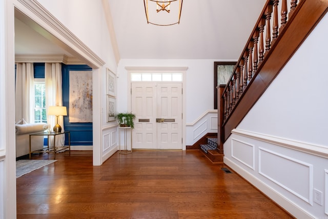 foyer with a decorative wall, stairway, wood finished floors, wainscoting, and high vaulted ceiling