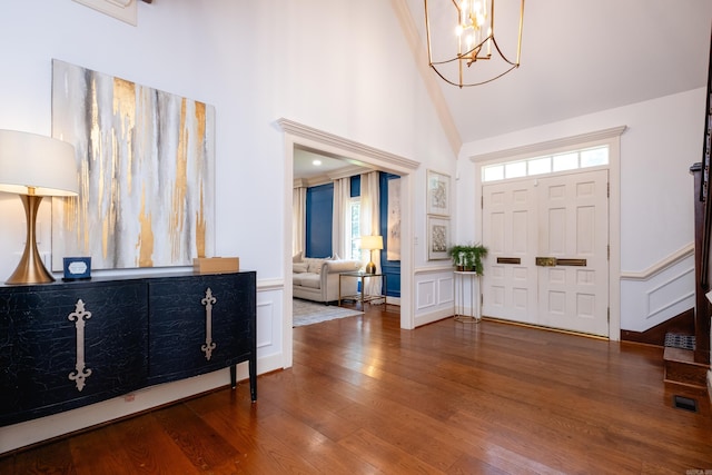 entrance foyer with high vaulted ceiling, wood finished floors, a chandelier, a decorative wall, and wainscoting