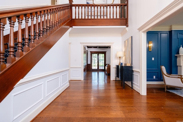 foyer with a decorative wall, wood finished floors, ornamental molding, a high ceiling, and french doors