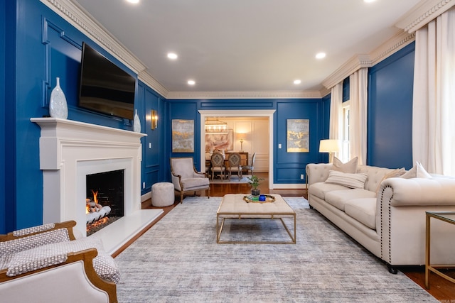 living room featuring ornamental molding, a decorative wall, a warm lit fireplace, recessed lighting, and wood finished floors