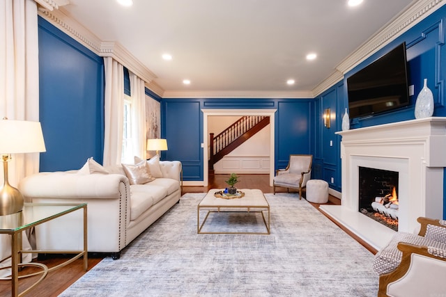 living area featuring ornamental molding, a decorative wall, wood finished floors, a lit fireplace, and recessed lighting