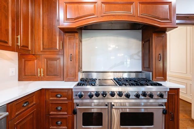 kitchen with double oven range, light countertops, brown cabinets, and custom range hood