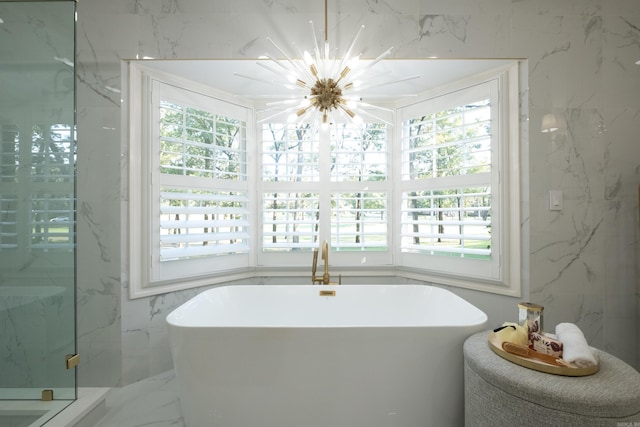 bathroom featuring marble tiled flooring, healthy amount of natural light, a freestanding bath, and a chandelier