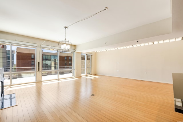 spare room with a chandelier, wood finished floors, and baseboards