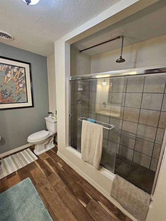 bathroom with a stall shower, toilet, wood finished floors, a textured ceiling, and baseboards