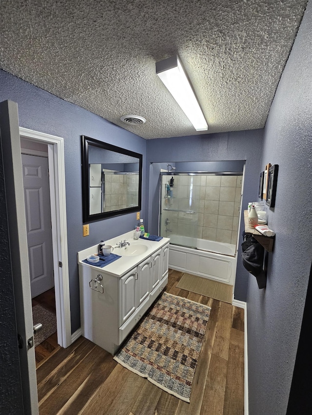 full bathroom with a textured wall, wood finished floors, a textured ceiling, shower / bath combination with glass door, and vanity