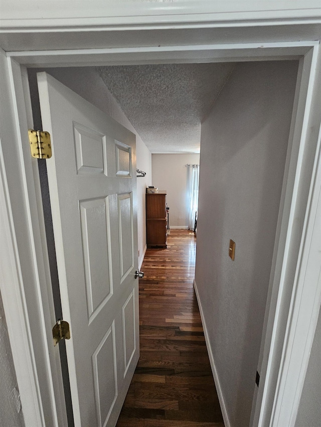 corridor featuring dark wood-type flooring, baseboards, and a textured ceiling