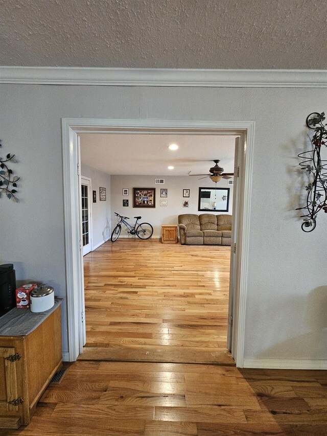 hallway with a textured ceiling, ornamental molding, wood finished floors, and baseboards