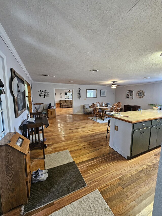living room featuring light wood-type flooring, a textured ceiling, crown molding, and ceiling fan