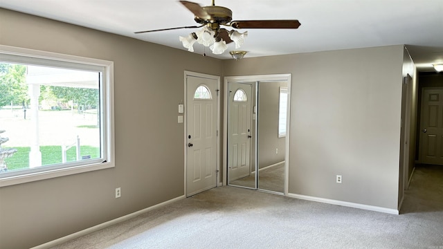 carpeted entryway with healthy amount of natural light, a ceiling fan, and baseboards