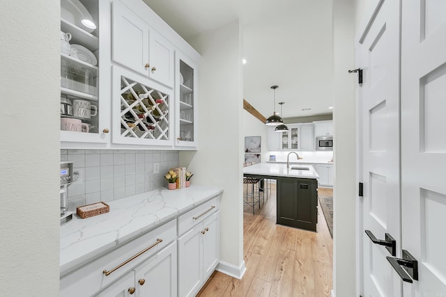 bar with a sink, stainless steel microwave, light wood-style floors, decorative backsplash, and hanging light fixtures