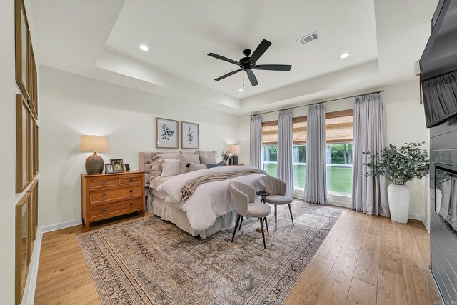 bedroom featuring a tray ceiling, light wood-style flooring, baseboards, recessed lighting, and ceiling fan