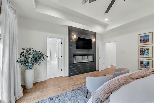 bedroom with a raised ceiling, a large fireplace, recessed lighting, light wood-style flooring, and baseboards