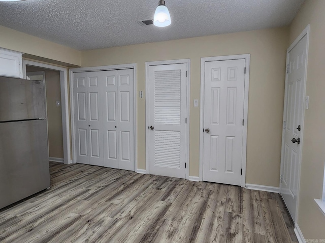 1807 Reservoir, Little Rock, AR 72227 - unfurnished bedroom with freestanding refrigerator, wood finished floors, multiple closets, and a textured ceiling