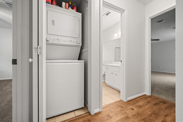 1121 Twin Pts Unit 1121C, Hot Springs, AR 71913 - washroom featuring stacked washer and clothes dryer, a textured ceiling, light wood finished floors, baseboards, and light colored carpet