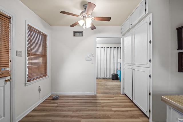 unfurnished dining area with ceiling fan, light wood-style flooring, and baseboards