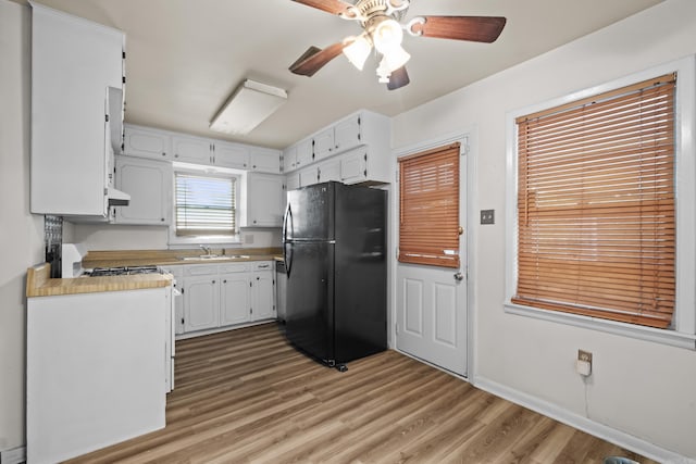 kitchen featuring freestanding refrigerator, a sink, gas range, ceiling fan, and light wood-style flooring